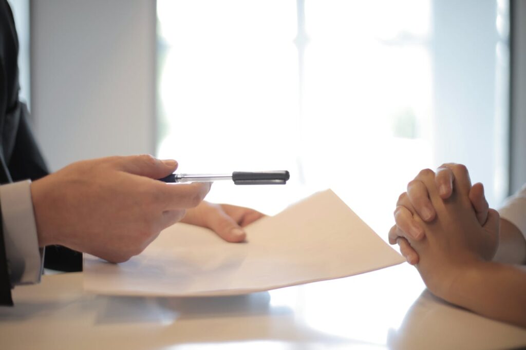 person holding pen and paper and person with hands crossed